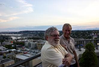 Two men standing on a balcony overlooking the city.