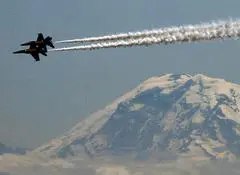 A jet flying in front of a mountain with smoke coming out.