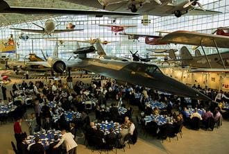 A large group of people sitting at tables in front of airplanes.